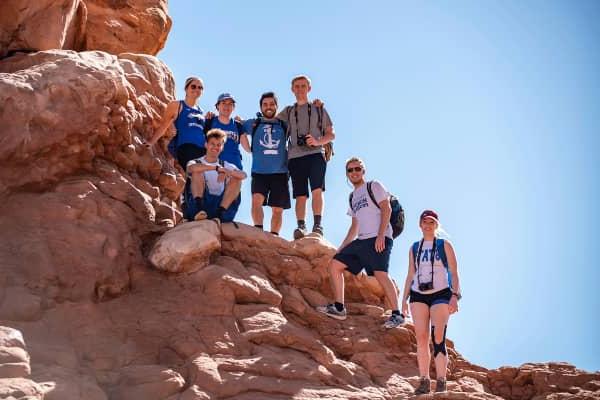 A group of students stand and pose for a photo on a large rock in a Utah national park.